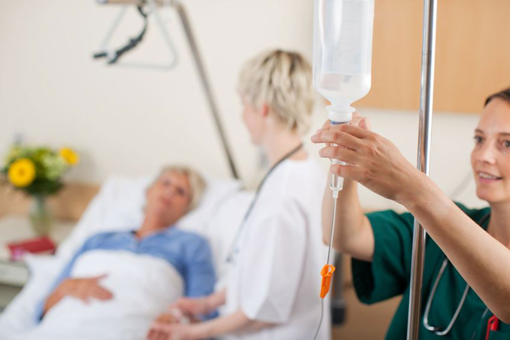 Nurse adjusting infusion bottle with doctor and patient in background in hospital