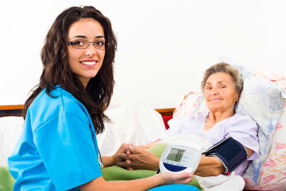 Kind nurse measuring elderly patient's blood pressure at home.