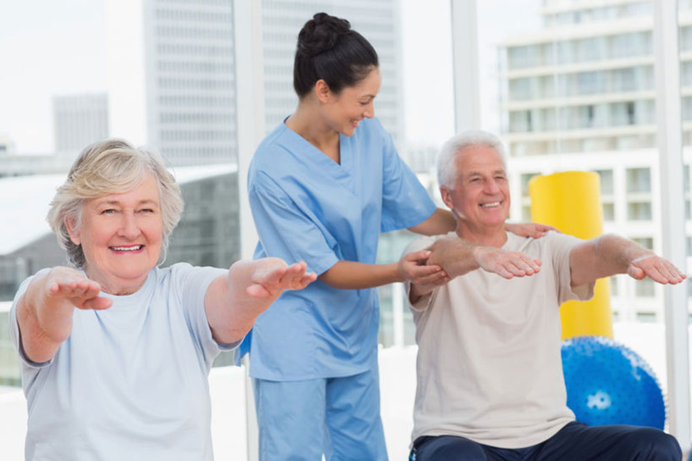 Happy young trainer assisting senior couple in exercising at gym