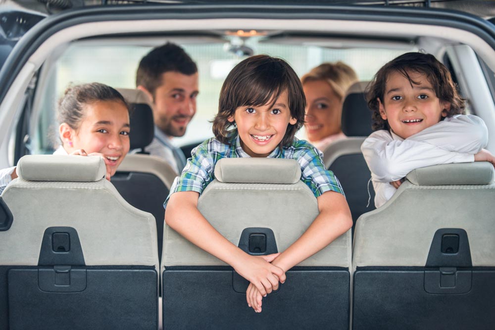 Playful kids posing in the back of a car with their parents in background