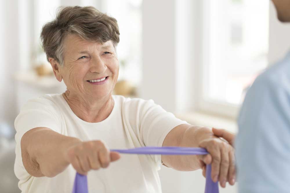 Smiling senior woman doing strength exercise with elastic band during fitness class